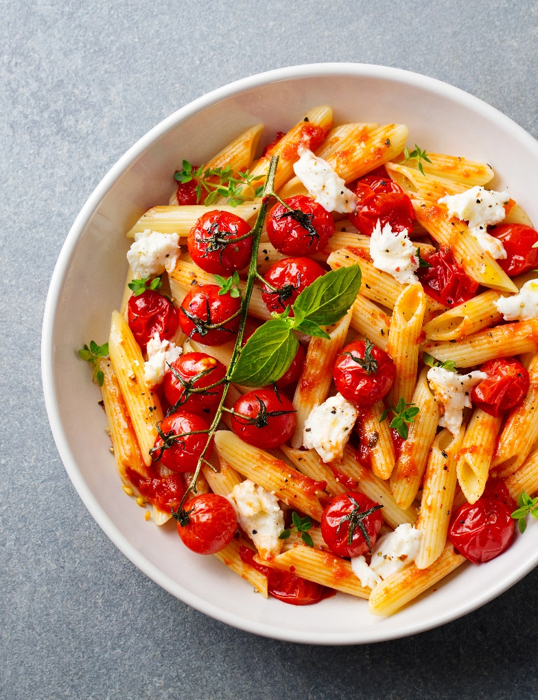 A bowl of fresh pasta with veggies and tomato sauce.