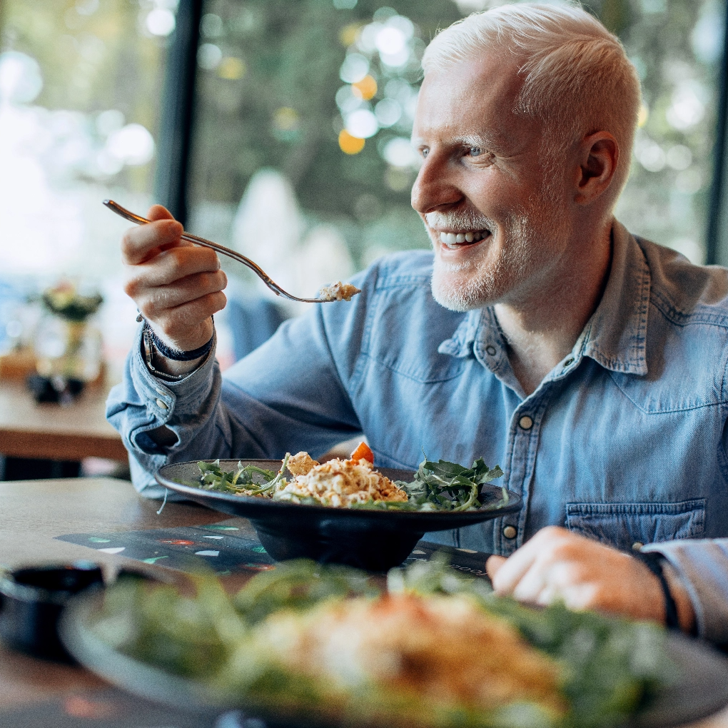 A man eats from a bowl full of fresh food and veggies.