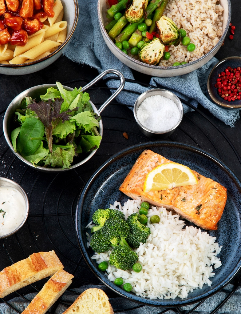 Healthy food including salmon, rice, greens and other veggies in various dishes on a table.