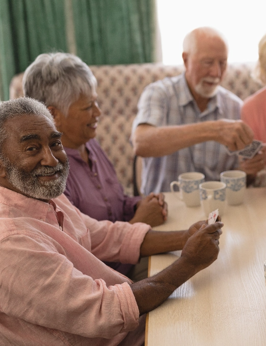 Several senior living residents play cards around a table in a common area.