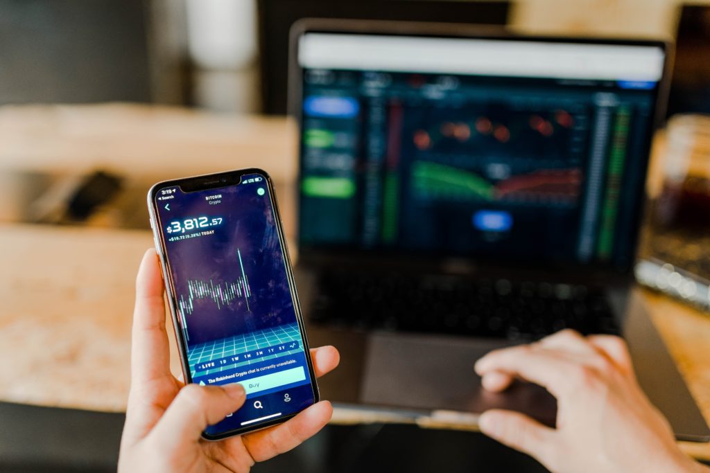 A person reviews financial statistics on their phone and laptop.
