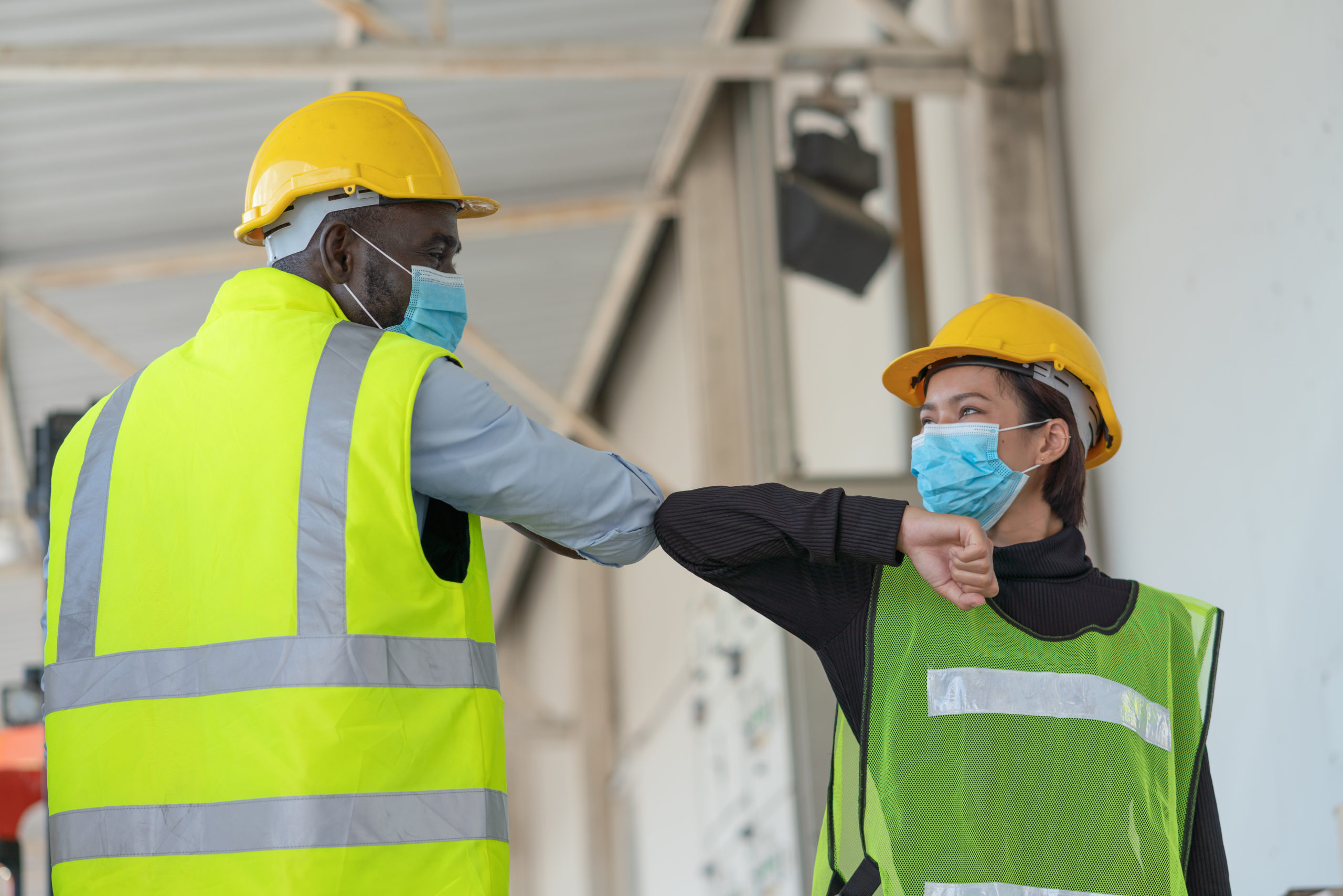 man and woman in construction vests touching elbows