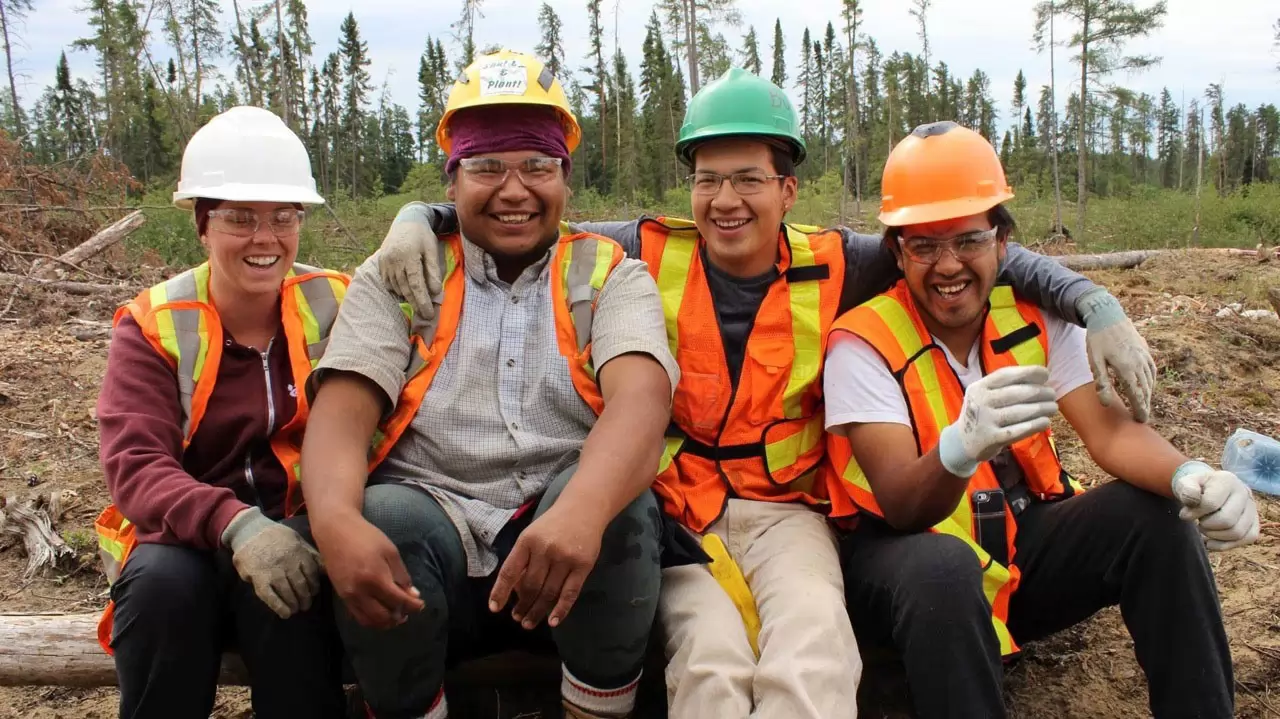 Group of construction workers standing in front of a forest wearing hard hats and safety vests